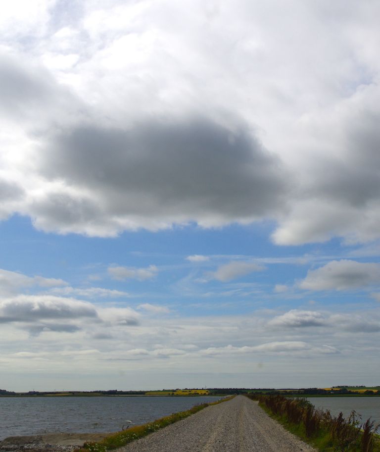 Kiesweg auf einem Damm durch das Wasser unter wolkenverhangenem Himmel. Gelassenheit. Weitsicht